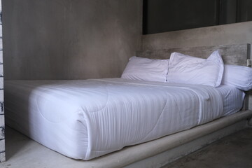 Simple and clean bed setup with white bedding placed on a built-in concrete platform inside an...