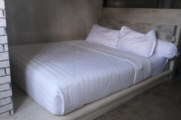 Cozy white bed with clean linens in a minimalist concrete bedroom, perfect for design inspiration,...