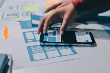 UX UI designer testing prototype on a phone, discussing and brainstorming on wireframes for a website and mobile app prototype, in the concept of website and mobile application design concept.