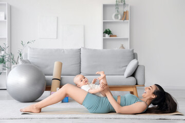 Sporty young woman with her little baby practicing yoga on mat at home