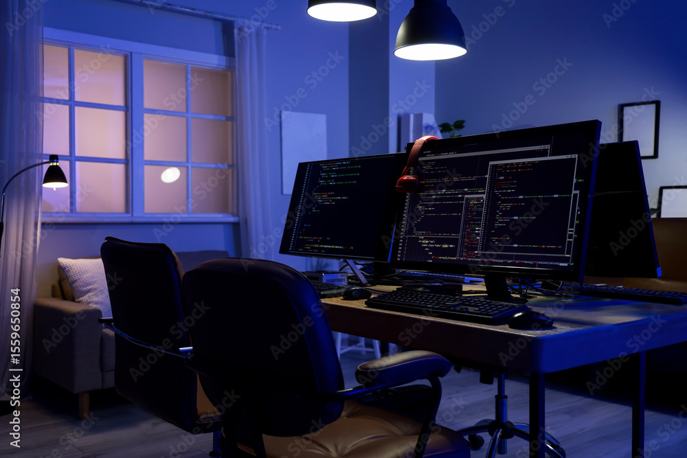 Poster programmer's desk with computer monitors and glowing lamps in dark office at night