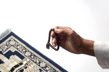 Hand holding prayer beads over a prayer mat, symbolizing Islamic worship and spirituality