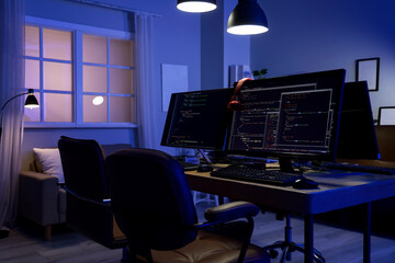 Programmer's desk with computer monitors and glowing lamps in dark office at night