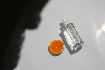 a clear dropper bottle containing liquid with small bubbles lies next to a half-cut orange on a...