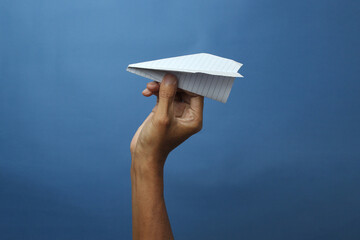 A hand holds a classic paper airplane, ready for flight against a solid blue background