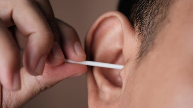 Southeast Asian Man cleaning ear with cotton swab closeup, personal hygiene