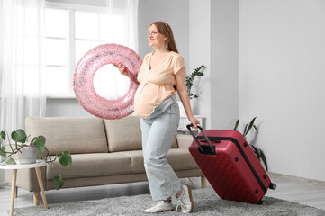 Young pregnant woman with suitcase and inflatable ring at home