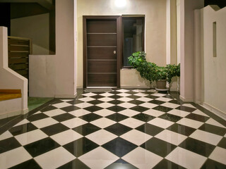 Modern entrance featuring a wooden door with horizontal metal strips, window, and potted plant. The floor is adorned with black and white checkered pattern, and space is illuminated by ceiling light.