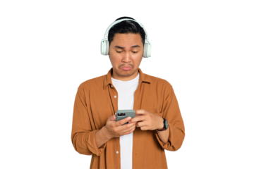 Young Asian man in casual shirt with headphones reading news on smartphone with sad expression isolated on transparent background