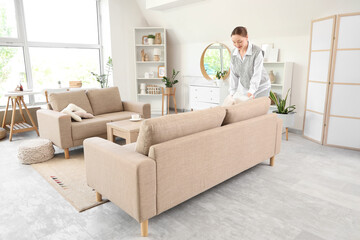 Young woman adjusting cushion on grey sofa in living room