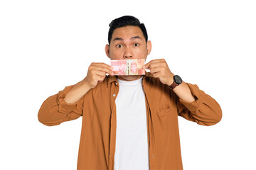 Bribery concept. Shocked young Asian man in casual shirt covering mouth with money isolated on...