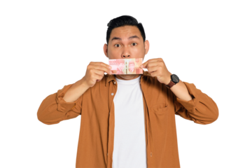 Bribery concept. Shocked young Asian man in casual shirt covering mouth with money isolated on transparent background