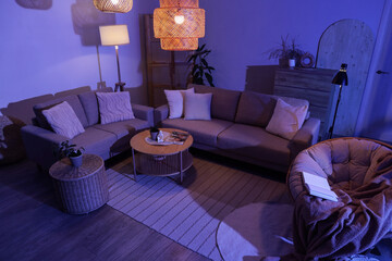 Interior of stylish living room with cozy grey sofas, coffee table and glowing lamps at night