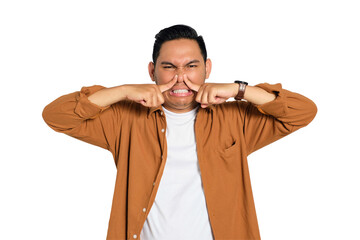 Young Asian man in casual shirt holding breath with finger on nose, smelling something stinky and...