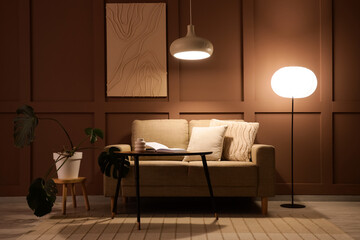 Interior of stylish living room with cozy sofa, coffee table and glowing lamps at evening