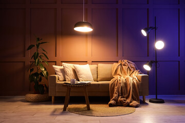 Interior of stylish living room with cozy sofa, coffee table and glowing lamps at evening