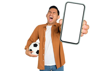 Excited young Asian man in casual shirt holding soccer ball and smartphone with blank screen, celebrating his victory isolated on transparent background