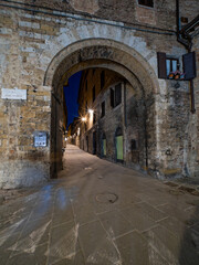 Le due porte alley in Siena, illuminated by a classic street light, creating a dramatic interplay of shadows and warm golden tones against historic stone walls. Travel in Tuscany, Italy.