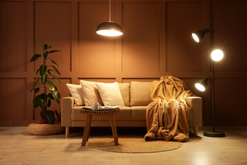 Interior of stylish living room with cozy sofa, coffee table and glowing lamps at evening
