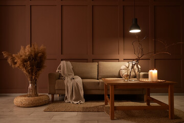 Interior of stylish living room with cozy grey sofa, coffee table, pampas grass and glowing lamps at evening