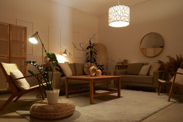 Interior of stylish living room with cozy grey sofas, armchairs, coffee table and glowing lamps at...