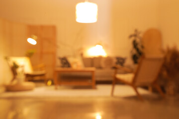 Blurred view of stylish living room with cozy grey sofas, armchairs, coffee table and glowing lamps at evening
