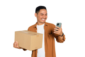 Happy young Asian man in casual shirt holding cardboard box and using mobile phone for online...