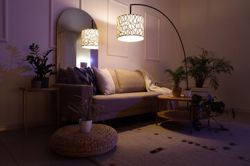 Interior of stylish living room with cozy grey sofa, coffee table, houseplants and glowing lamps at...