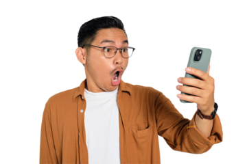 Surprised young Asian man in casual shirt using mobile phone with open mouth, reading great news message isolated on transparent background