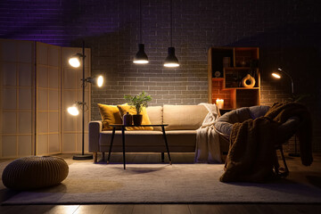 Interior of stylish living room with cozy grey sofa, armchair, coffee table and glowing lamps at...