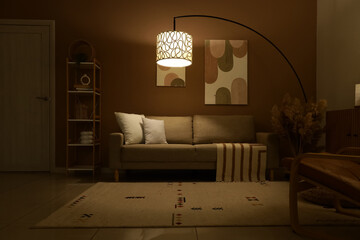 Interior of stylish living room with cozy sofa, pampas grass and glowing lamp at evening
