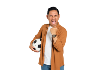 Excited young Asian man in casual shirt holding soccer ball, screaming with mouth wide open, celebrating victory isolated on transparent background