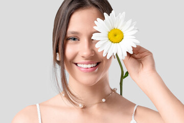Happy young woman with chamomile flower on grey background, closeup