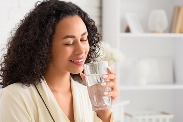 Young African-American woman drinking water in bedroom, closeup