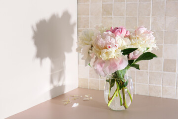 Vase with beautiful peony flowers on table near pink tile wall