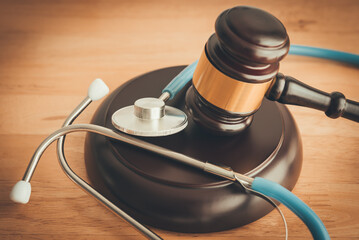 Judge hammer gavel and doctor stethoscope on wooden table background in courtroom. Health law,...
