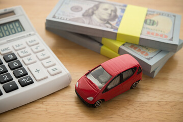Simple car toy, stack US dollar banknotes and calculator on wooden table. Money savings management for buying new or used car, car loan payment, insurance, tax, car for cash and so on concept.