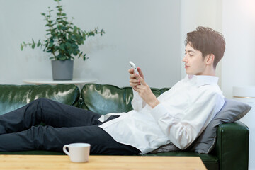 ソファでくつろぎながらスマートフォンを操作する男性