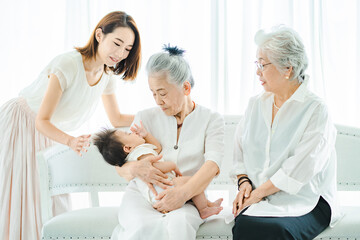 赤ちゃんを抱っこするシニア女性と見守る女性たち