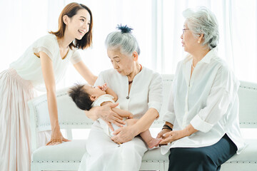 赤ちゃんを抱っこするシニア女性と見守る女性たち