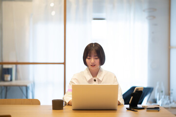 自宅の部屋でノートPCを操作する若い女性