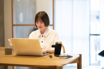 自宅の部屋でノートPCを操作する若い女性