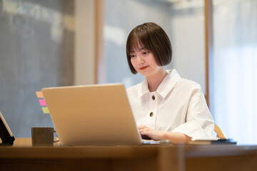 自宅の部屋でノートPCを操作する若い女性