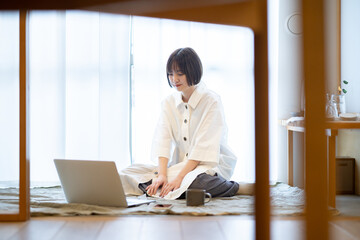 自宅の部屋でリラックスした雰囲気でノートPCを見る女性