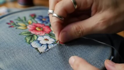 Close-up of a hand embroidering colorful floral patterns on denim fabric, showcasing intricate craftsmanship - Powered by Adobe