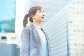 ビル街で空を見上げる若い女性