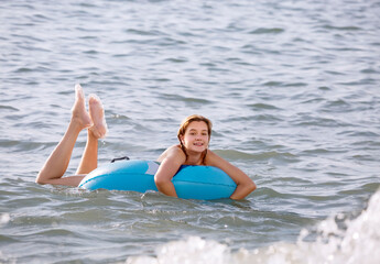 A cheerful young girl swims with an inflatable circle in the sea