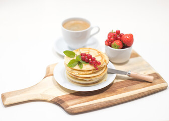 Plate with Pancakes and Red Currants on Wooden Board with Strawberries and Coffee in Background