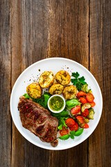 Grilled beef steak with baked potatoes and fresh salad on wooden table	