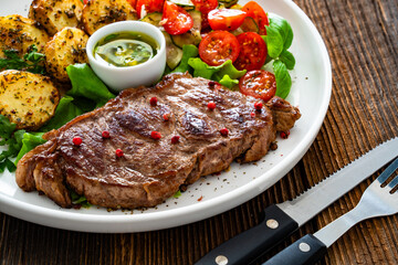 Grilled beef steak with baked potatoes and fresh salad on wooden table	